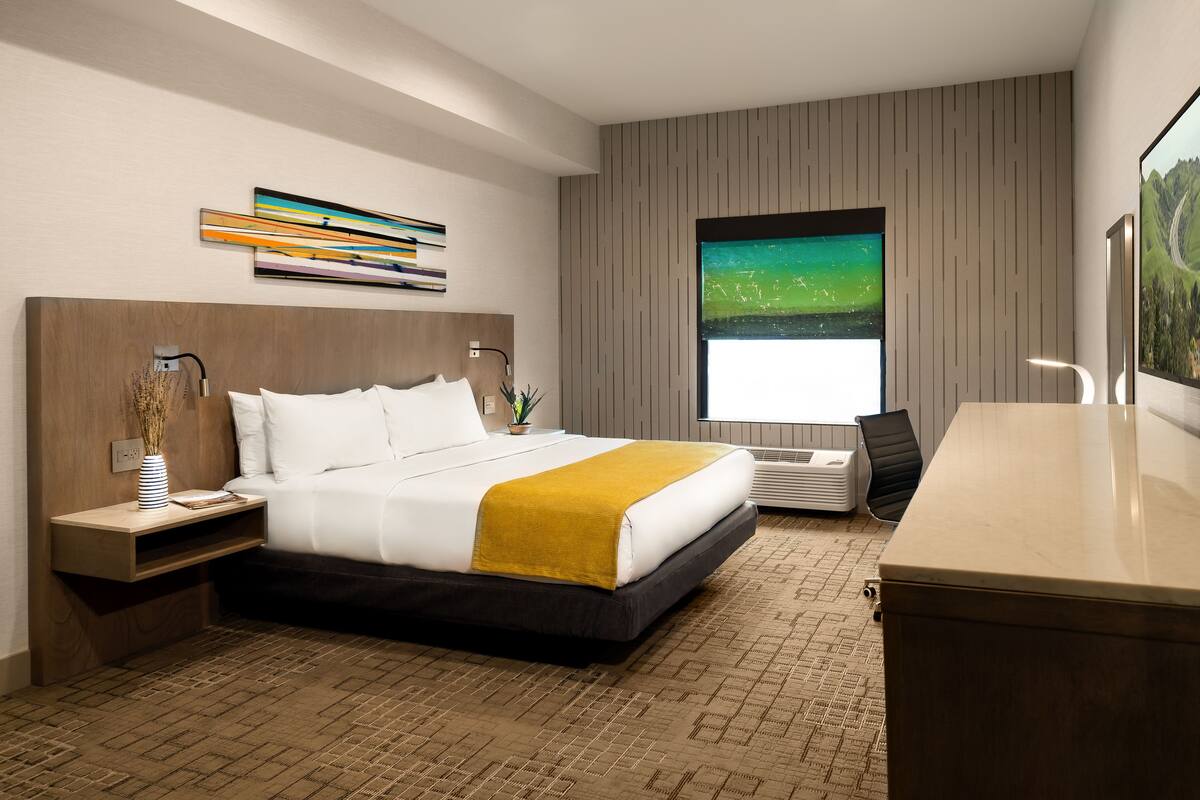 Une chambre d’hôtel moderne dotée d’un grand lit, d’un bureau, d’une fenêtre offrant une vue agréable et d’un élément décoratif mural.