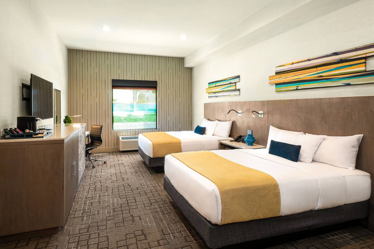 Une chambre d’hôtel avec deux lits, un bureau, une télévision et une grande fenêtre donnant sur l’extérieur.