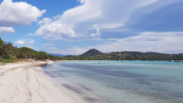 Une plage à l’eau turquoise et limpide, un rivage sablonneux et une montagne en arrière-plan.