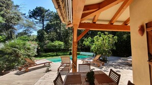 Une terrasse extérieure aménagée avec des meubles en bois, une piscine et une végétation luxuriante.