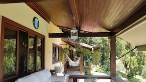 A covered outdoor seating area with a white sofa and a small table, surrounded by potted plants and a hammock. - Vista paradisiaca (Angra dos Reis)
