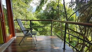 A wooden deck with a metal railing, a single chair, and lush greenery in the background. - Paradise Garden Resort (Yatiyantota)