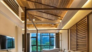 Un dormitorio moderno con una cama grande, vigas de madera en el techo, un televisor y vistas al exterior.