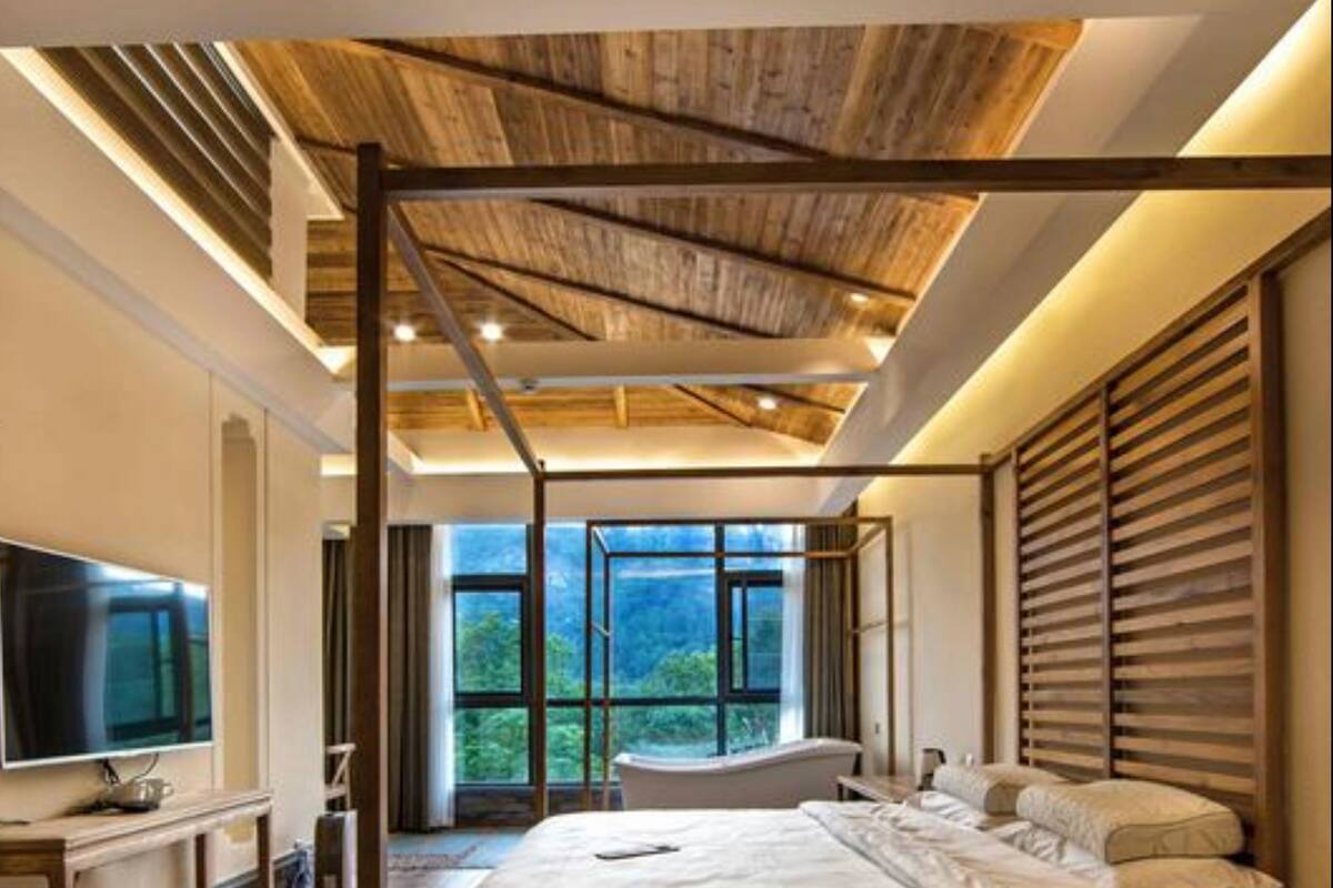A modern bedroom with a large bed, wooden ceiling beams, a TV, and a view of the outdoors.