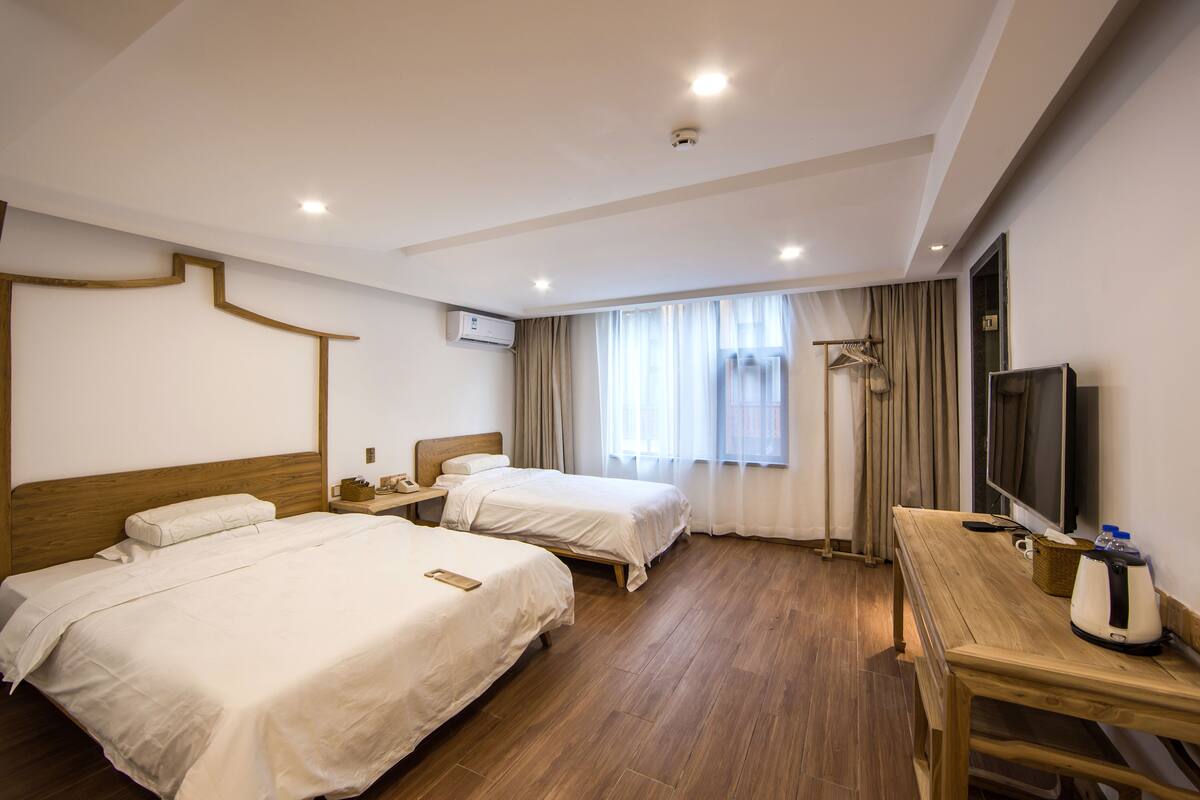 A hotel room with two beds, a wooden desk, a television, and a window with curtains.