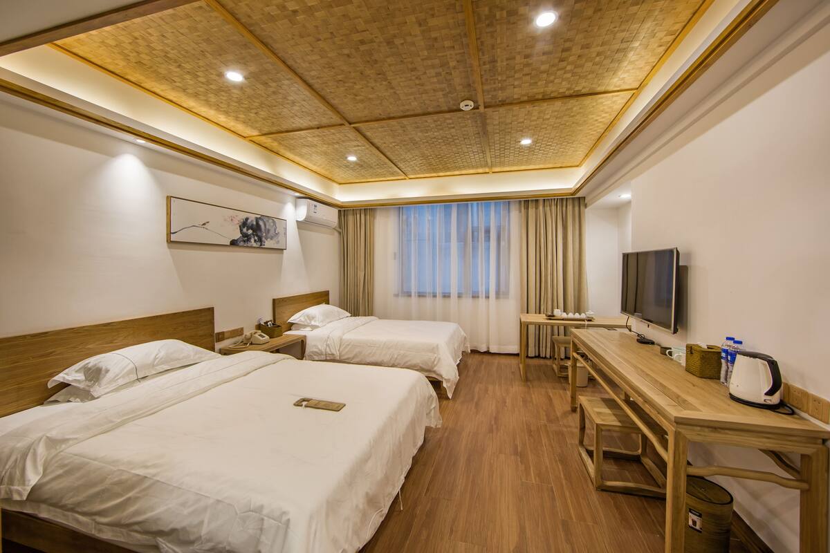 A hotel room with two beds, a wooden desk, a television, and a window with curtains.