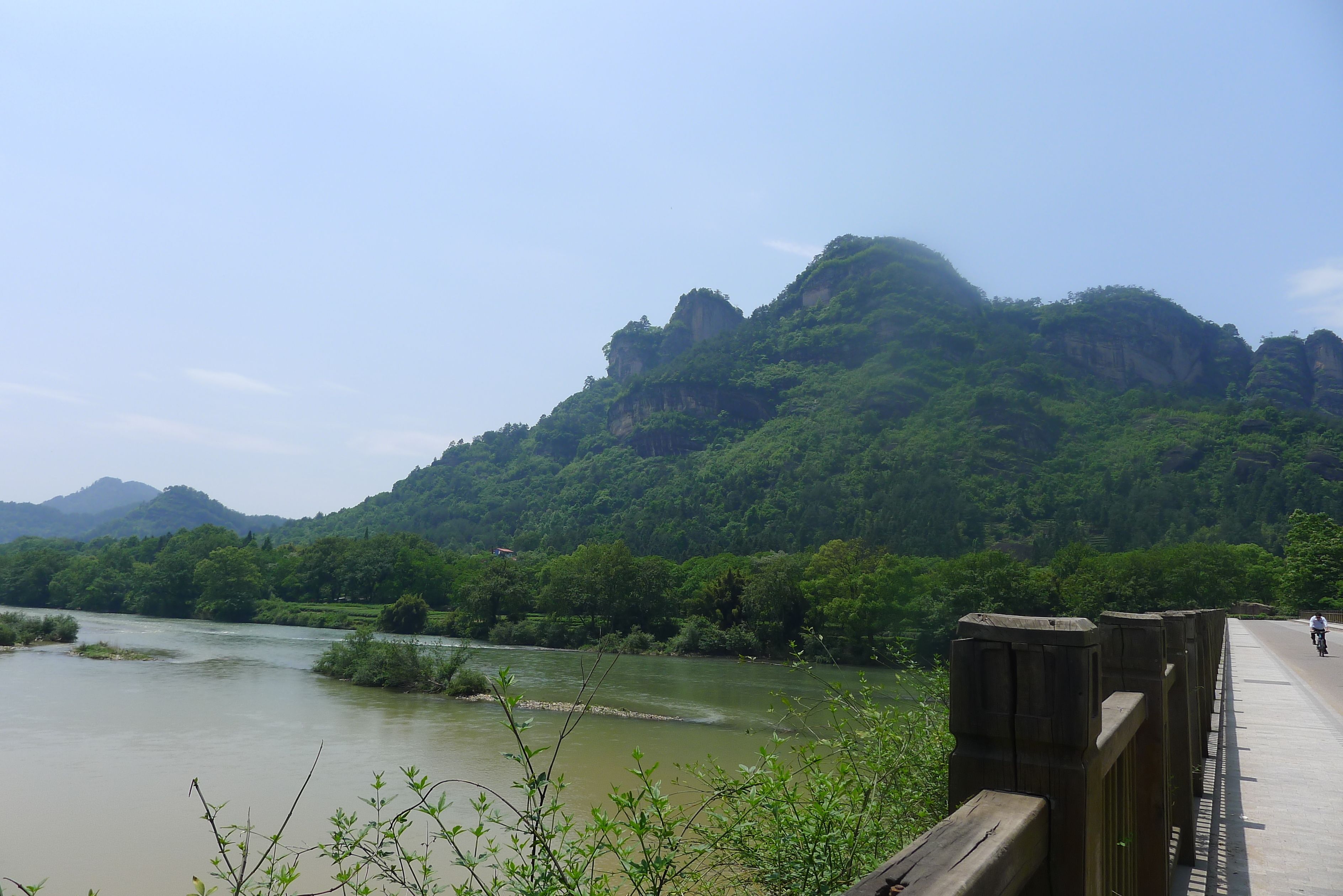 A river with a bridge and a forested mountain in the background.