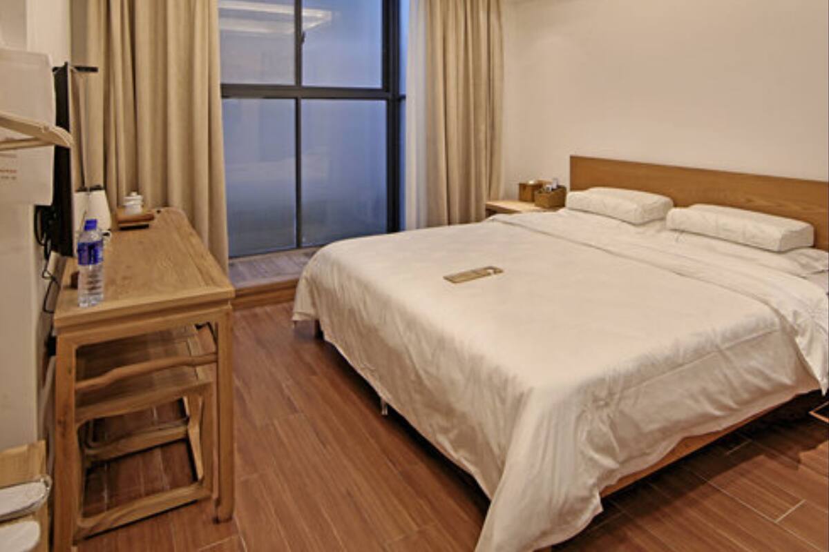 A hotel room with a bed, a desk, a chair, a nightstand, and a window with curtains.