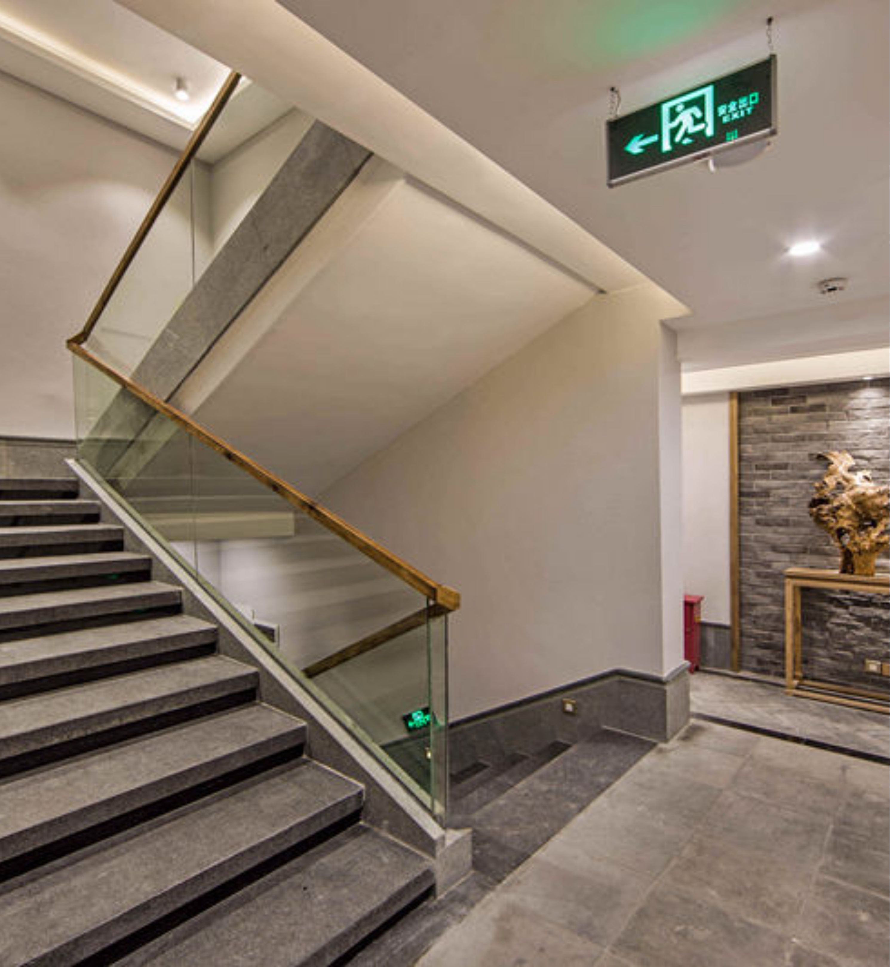 A modern staircase with glass railings and a sign indicating an exit.