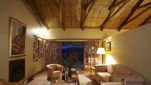 A cozy living room with a thatched ceiling, a fireplace, and a view of the night sky through a glass door. - Bushmanspad Estate (Boesmanspad)