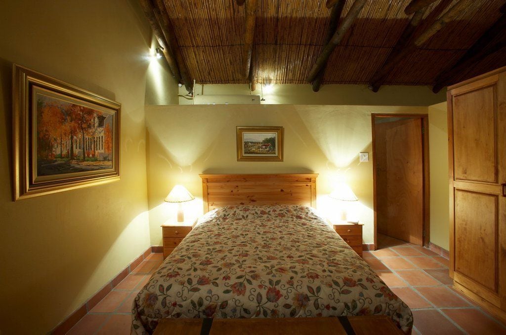 A bedroom with a wooden bed, two bedside lamps, a framed painting on the wall, and a wooden wardrobe.
