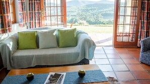 A cozy room with a sofa, a coffee table, and a view of a mountainous landscape through open doors. - Bushmanspad Estate (Boesmanspad)