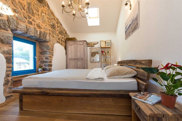 A bedroom with a stone wall, wooden bed, and a view through a window.