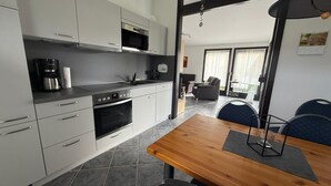 A modern kitchen with a wooden dining table, built-in appliances, and a view to a balcony. - Vacation home that offers rest and relaxation during every season (Niedersachsen)