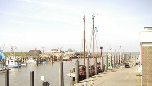 A marina with boats docked, a pedestrian walkway, and a building on the right. - Vacation home that offers rest and relaxation during every season (Niedersachsen)