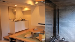 Un baño moderno con cabina de ducha de vidrio, tocador de madera y una pequeña zona de estar con cojines.