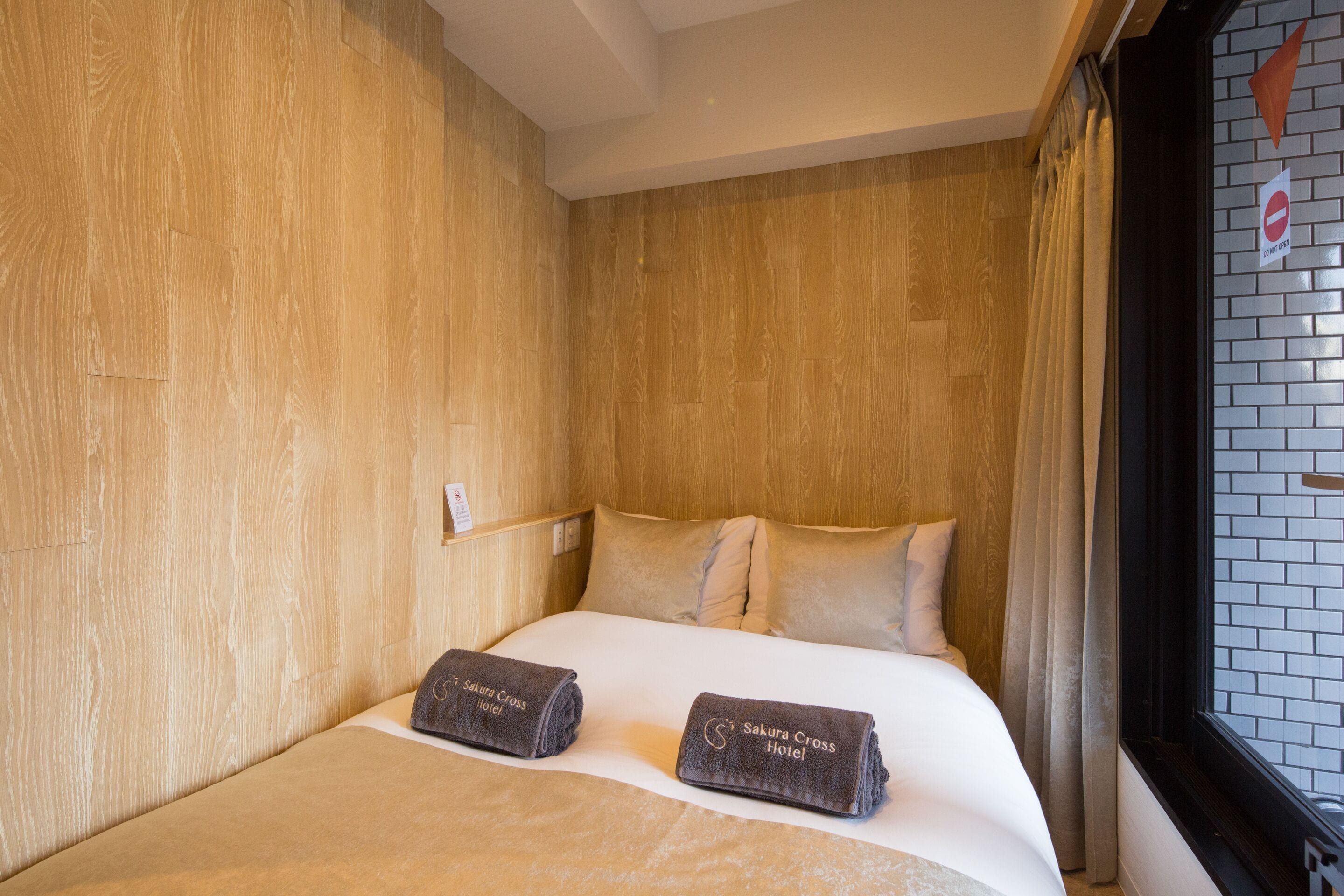 A hotel room with a wooden wall, a bed with two pillows, and a window with curtains.