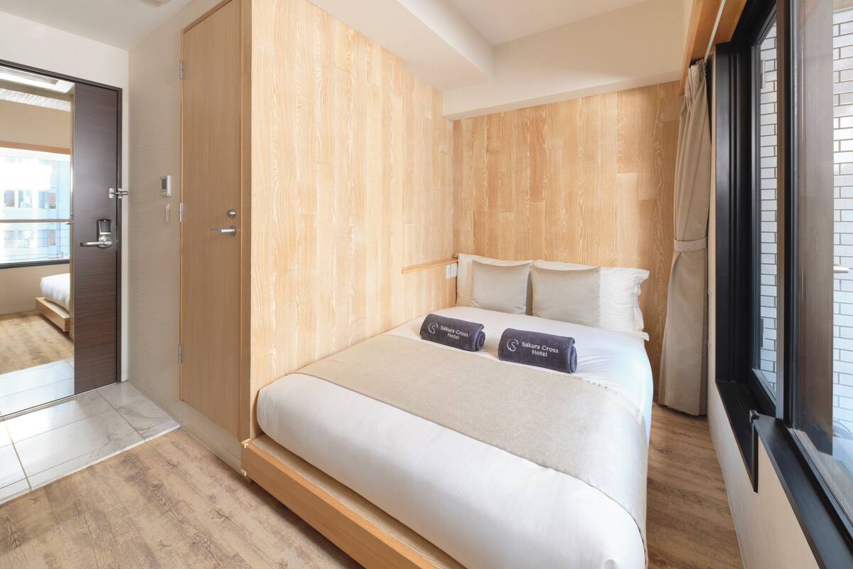 Habitación de hotel moderna con una cama grande, un armario de madera y vistas de la ciudad por la ventana.