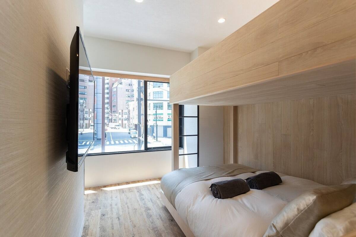 Un dormitorio moderno con un ventanal grande, una cama y un televisor montado.