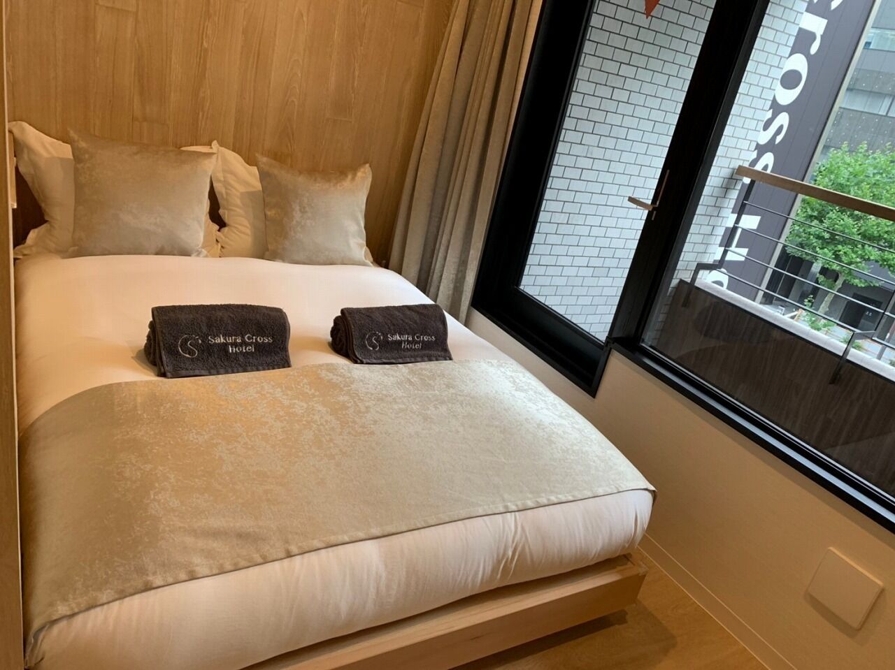 Hotellihuone, jossa on sänky, tyynyt, peitto ja hotellin nimellä varustetut pyyhkeet.