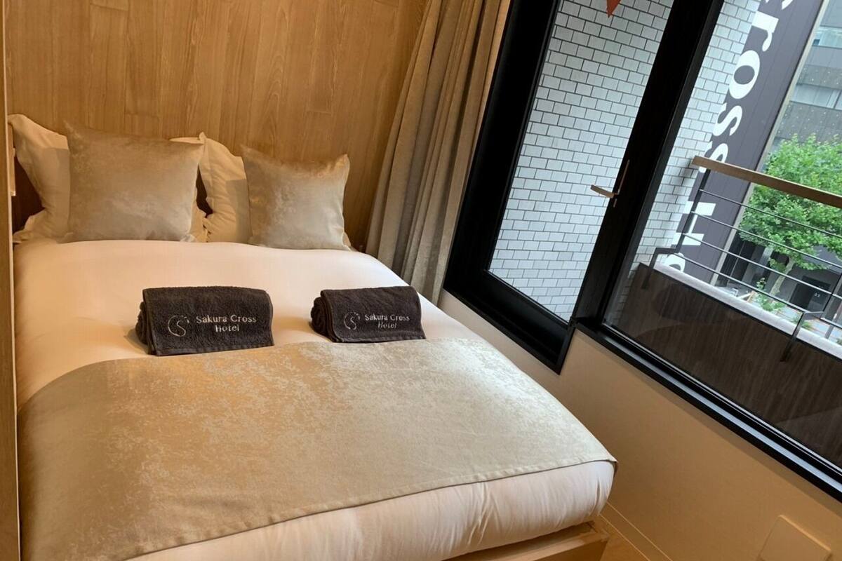 Habitación de hotel con cama, almohadas, una manta y toallas con el nombre del hotel.