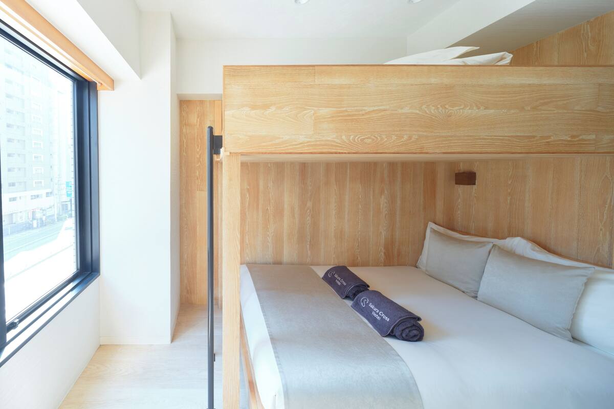 Habitación de hotel moderna con literas, una ventana con vista a la ciudad y una cama bien hecha con una toalla.