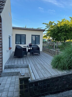 A patio with a table and chairs, a stone wall, and a wooden deck.