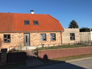 A brick house with a red-tiled roof, two windows, and a small porch.