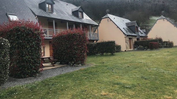 Una hilera de casas con techos inclinados, un césped y una montaña al fondo.