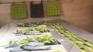 Un dormitorio con una cama cubierta por una colcha verde y blanca estampada, techo inclinado de madera y una pequeña decoración en la pared sobre la cama.