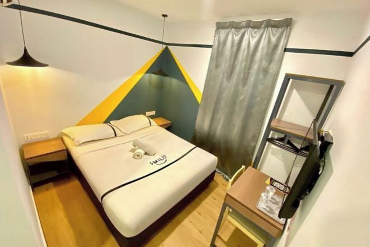 A hotel room with a bed, a bedside table, a mirror, and a curtain.