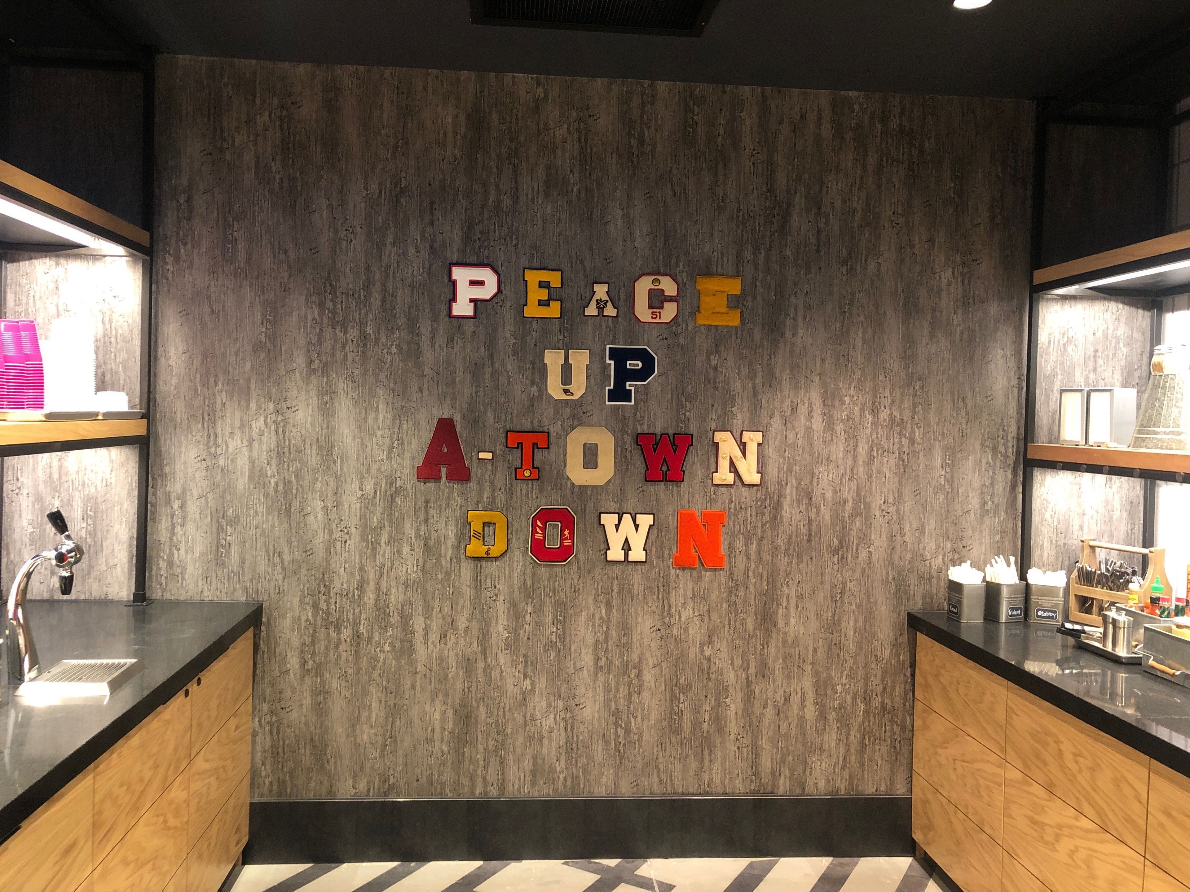 Eine moderne Küche mit Holzausstattung, einer schwarzen Arbeitsplatte und einer Wand mit dem Schriftzug 'PEACE UP ATOWN DOWN'.
