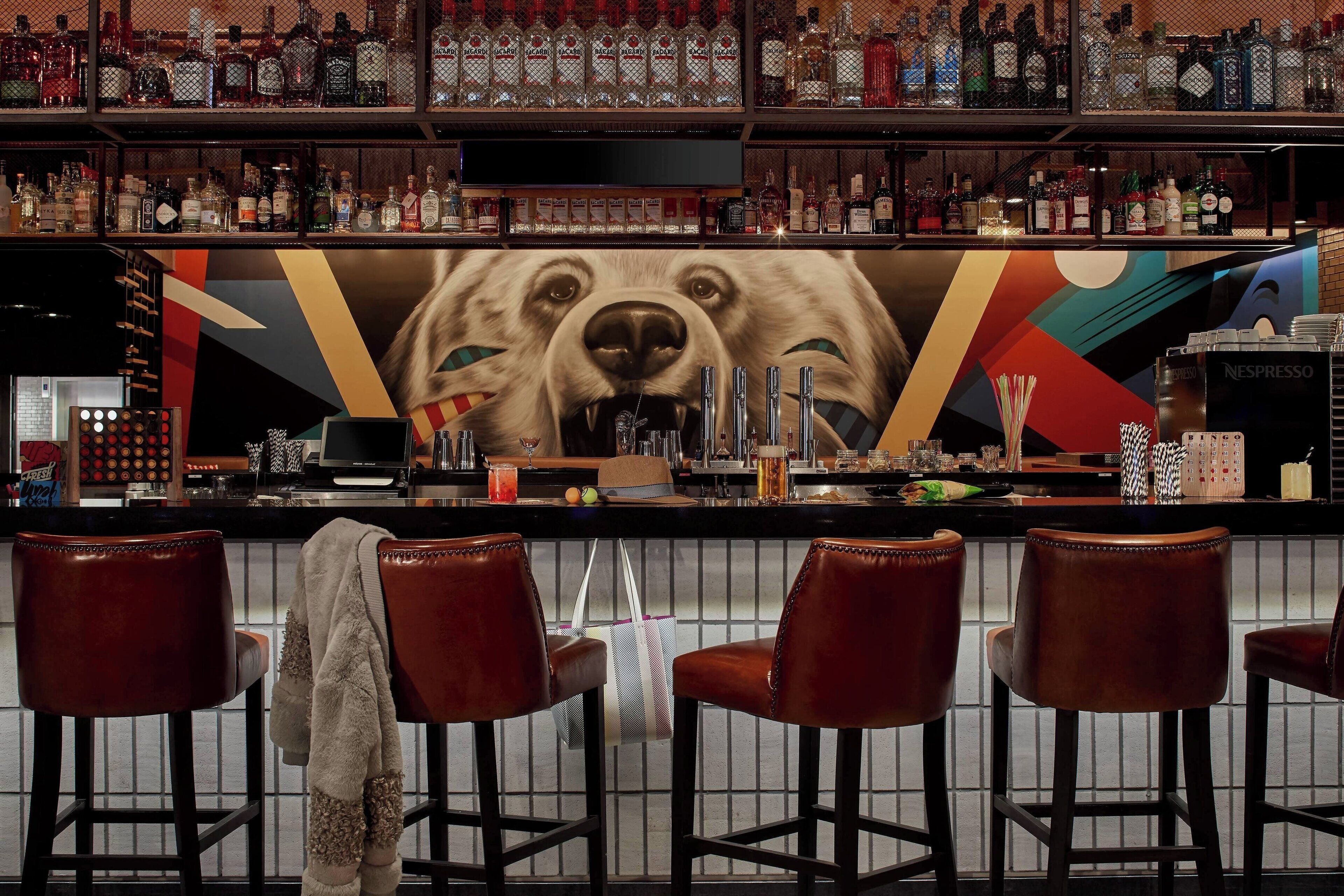 A bar area with a large bear mural, multiple liquor bottles, and bar stools.