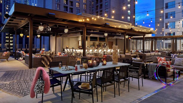 An outdoor seating area with tables and chairs, a bar, and a view of tall buildings in the background. - Moxy Atlanta Midtown (Atlanta)