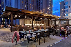 An outdoor seating area with tables and chairs, a bar, and a view of tall buildings in the background. - Moxy Atlanta Midtown (Atlanta)