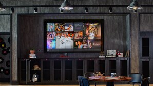 A modern interior with a large TV displaying various content, a wooden table with chairs, and a wall with a record collection. - Moxy Atlanta Midtown (Atlanta)