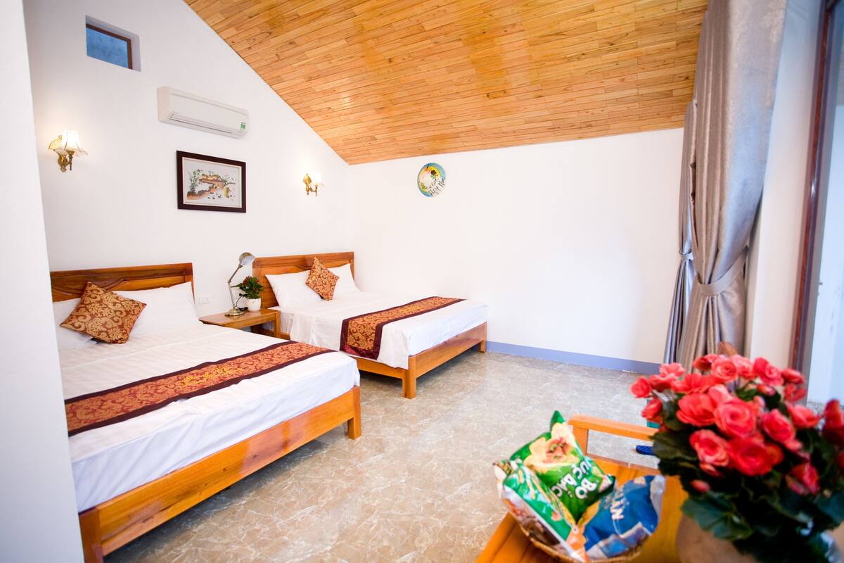 Una habitación con dos camas de madera, una mesita con un florero y un aire acondicionado instalado en la pared.