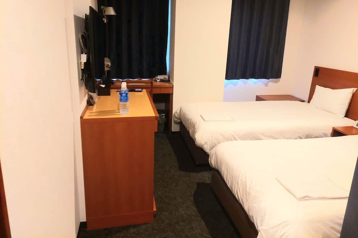 Une chambre d’hôtel avec deux lits, un bureau, une chaise, une lampe et une bouteille d’eau.