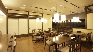 Un salón de conferencias con mesas y sillas de madera, iluminación empotrada y un ventanal grande.