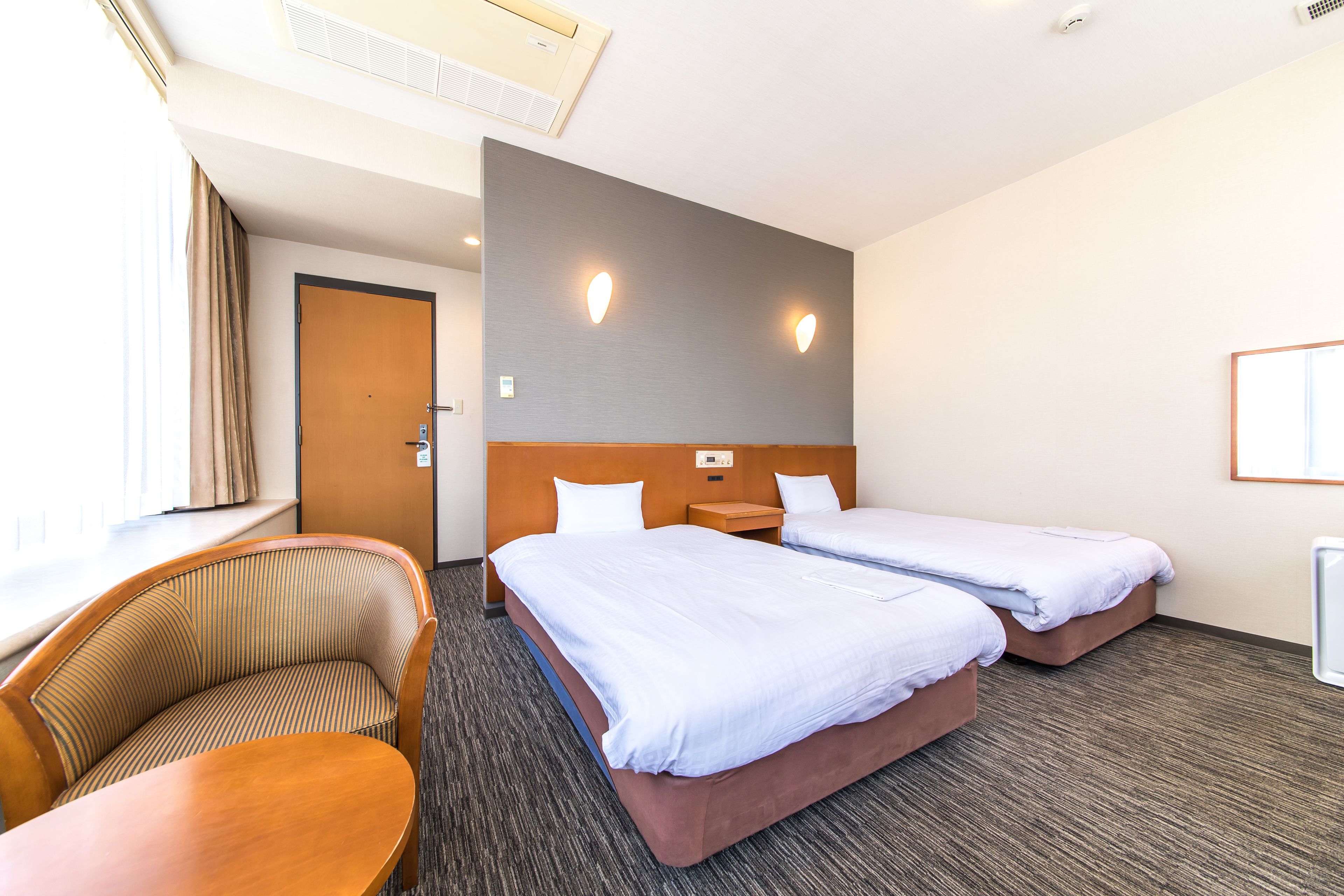 Quarto de hotel com duas camas, um sofá, uma mesa e uma janela com cortinas.