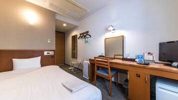 A hotel room with a bed, a desk, a chair, a small refrigerator, and a mirror.