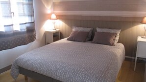 Een net opgemaakt bed met beddengoed met patroon, twee bedlampen en een raam met gordijnen.