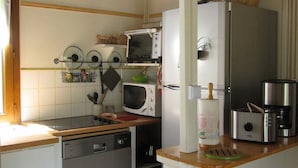 Een kleine keuken met een houten plafond, witte muren en een klein aanrecht. Er is een vaatwasser, een magnetron, een broodrooster en een koelkast aanwezig.