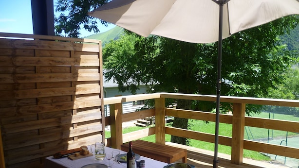 Een terras met een eettafel voor twee personen, een fles wijn en een saladekom.