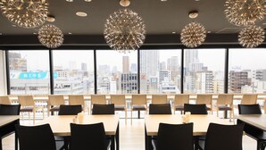 A modern dining area with multiple tables and chairs, large windows offering a city view, and geometric ceiling lights.