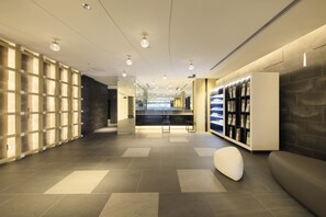 A modern hotel lobby with a reception desk, seating area, and a display of magazines. - S-Peria Inn Osaka Hommachi (Osaka)