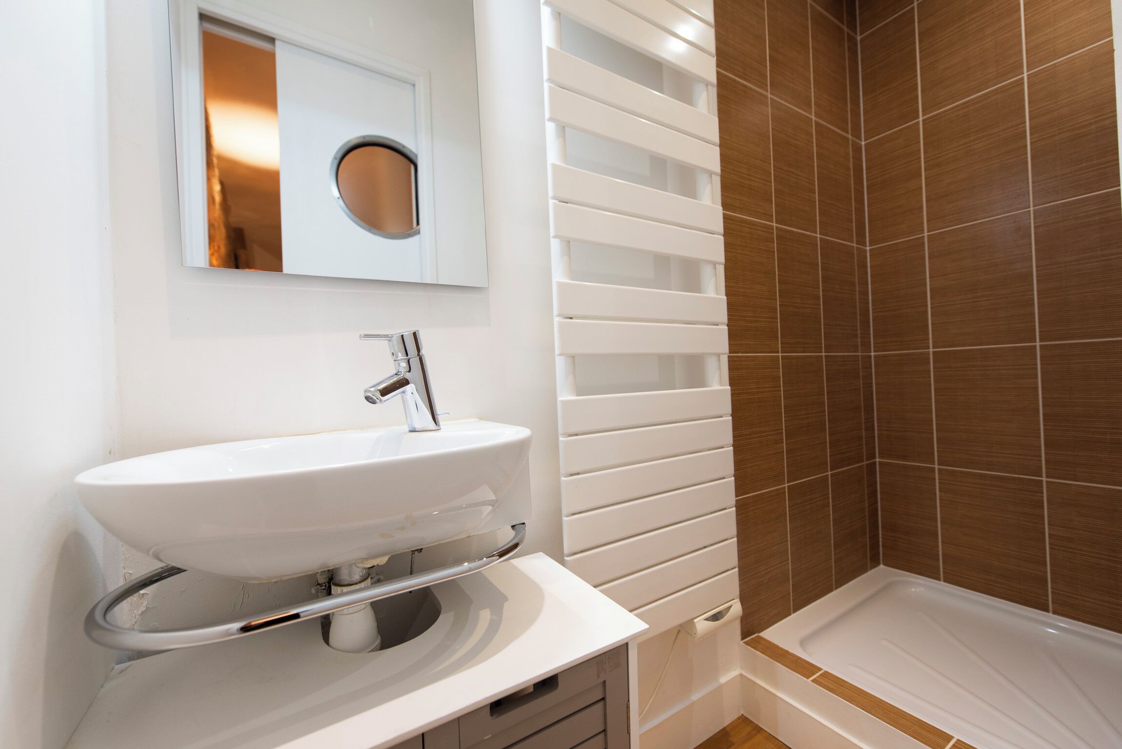 Ein Badezimmer mit Waschbecken, Spiegel, Dusche mit braunen Fliesen und einer weißen Badewanne.