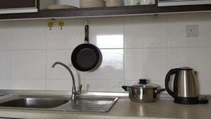 Una cocina con un lavamanos, una sartén, un hervidor y una olla.