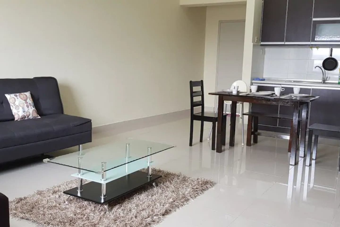 Un salon moderne avec une table basse en verre, un canapé foncé et un coin repas comprenant une table et des chaises.