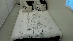 A bed with a floral bedspread, two pillows with leaf patterns, and a plain wall with a window.